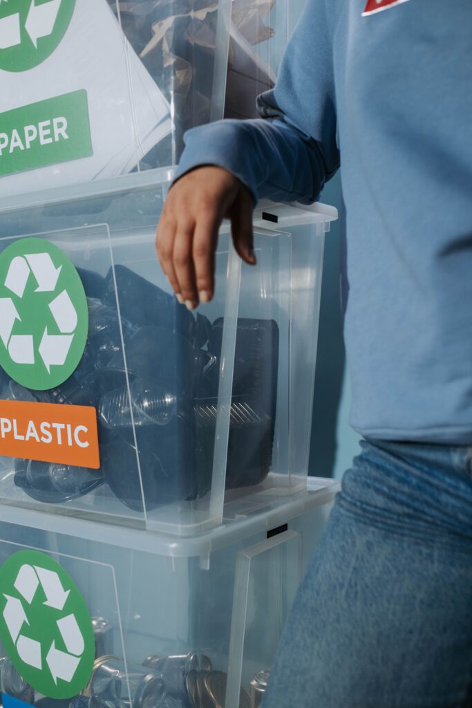 Close-up of labeled recycling bins for paper and plastic with person organizing.